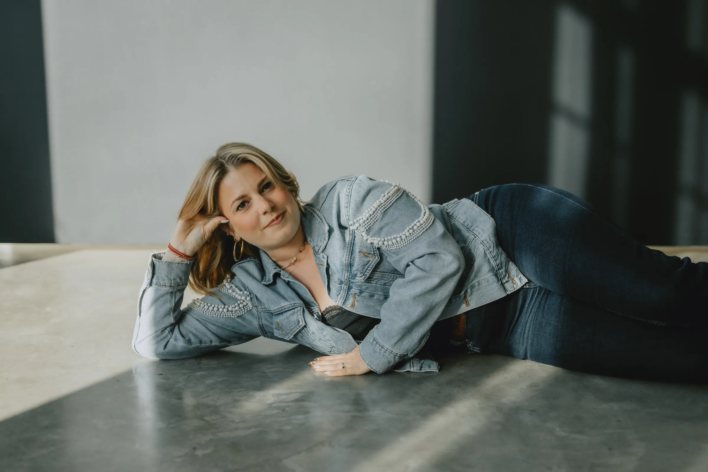 Clémence Tillerot lying on a studio floor in a denim jacket, smiling