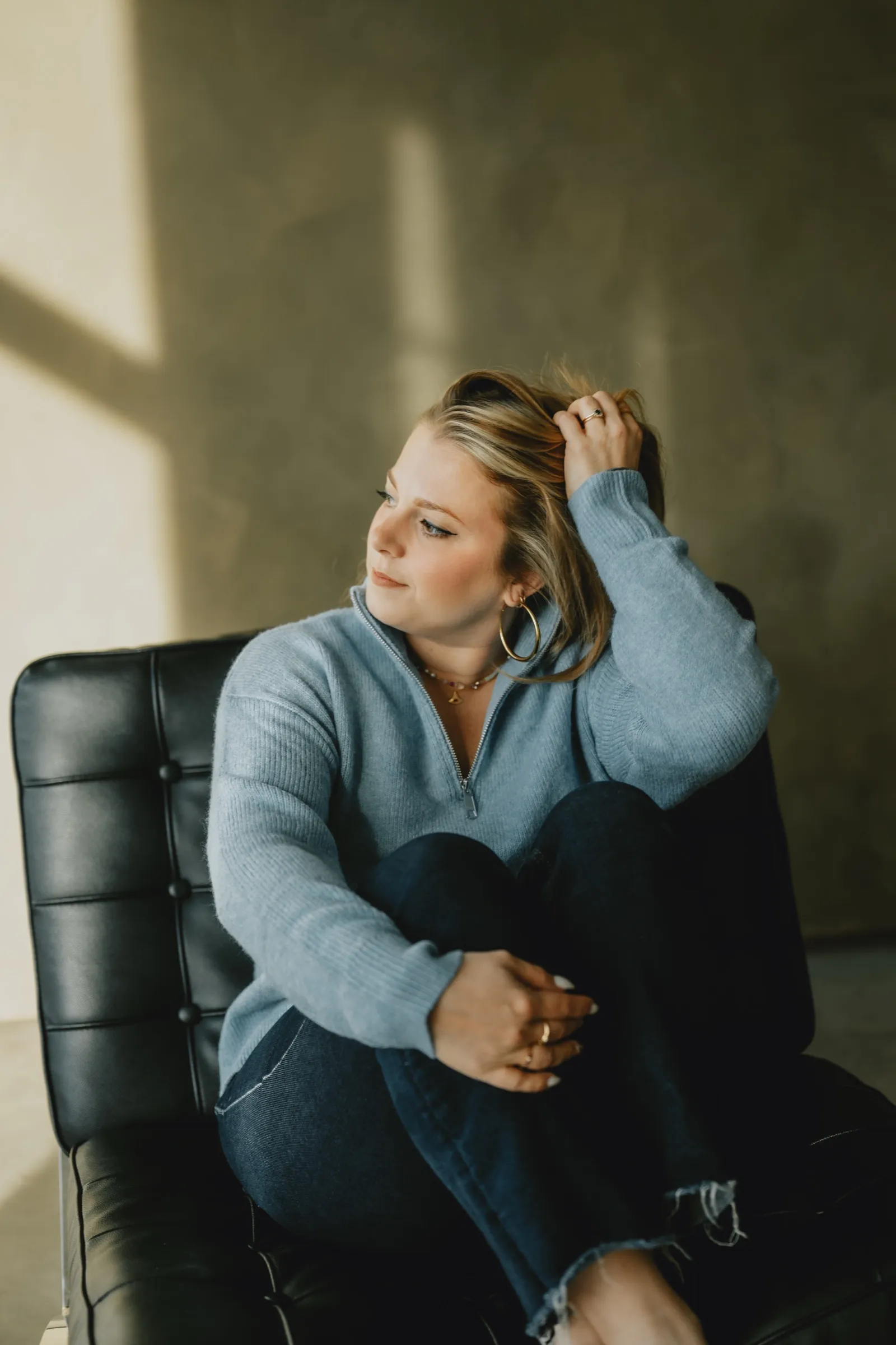 Clémence Tillerot in a blue sweater, sitting in a black armchair and looking away