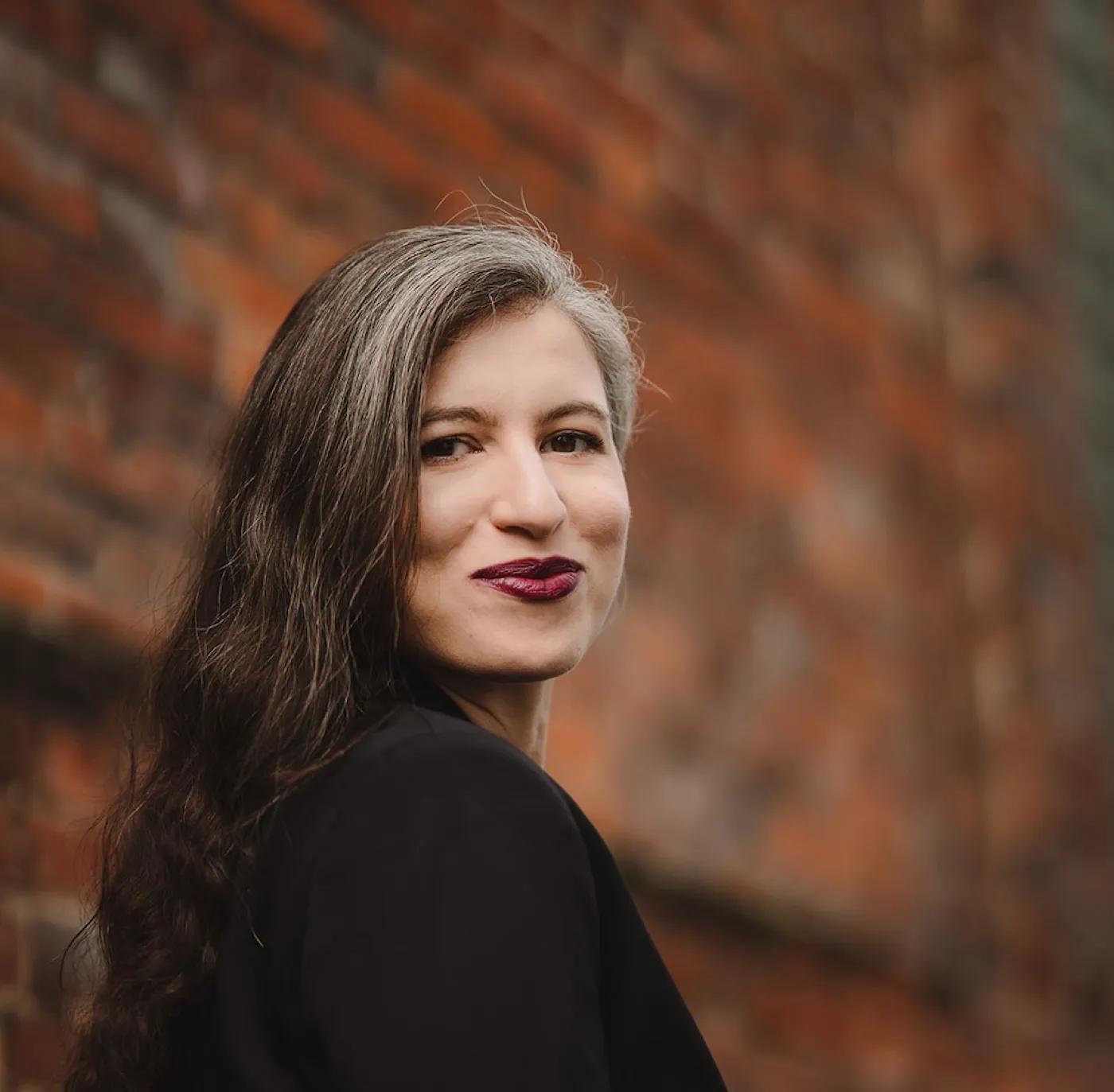 Sarah Zitouni, founder of PowHER ta carrière, in front of a brick wall