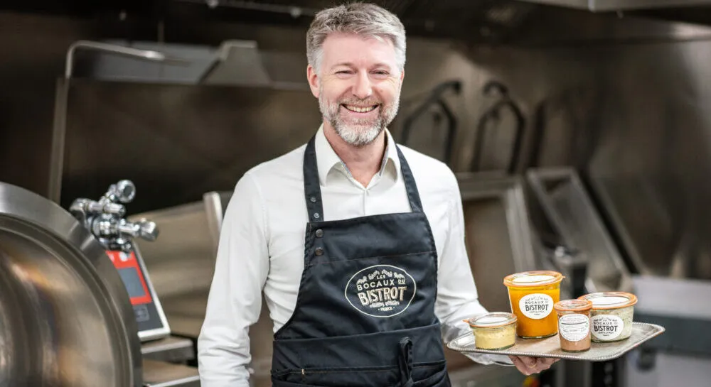 Sylvain, founder of Les Bocaux du Bistrot, holding a tray of jars in the kitchen